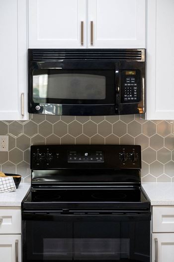 A kitchen with white cabinets and a black stove and microwave